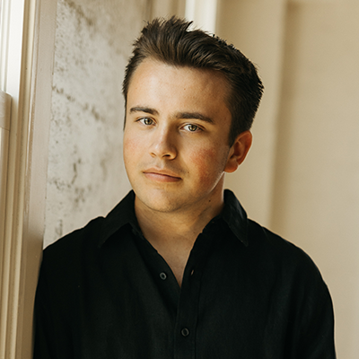 Young Musician Ryan Woodard poses against a window, wearing a black outfit