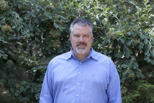 Man in blue button down against a green leafy background