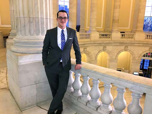 Smiling man in a suit, leaning on the 2nd floor railing in the US Capitol rotunda