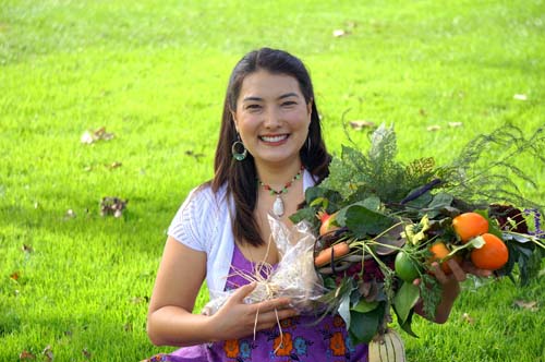 Seated, smiling woman holding a bouquet of fruits and vegetables