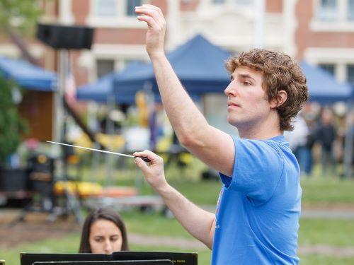 Man holding a baton, conducting an outdoor musical performance