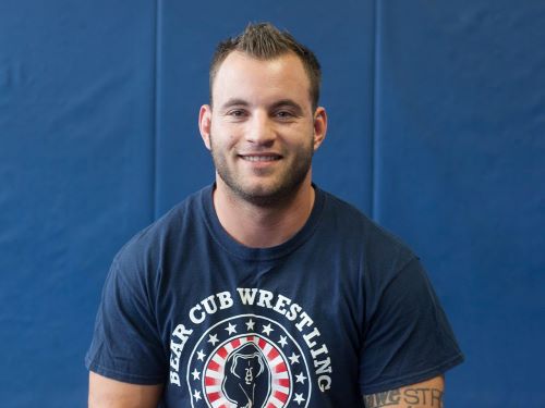 Head and shoulders portrait of a main in a blue tee shirt in front of a blue wall