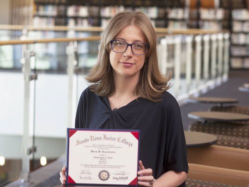 Portrait of a woman standing in a library, holding her SRJC diploma