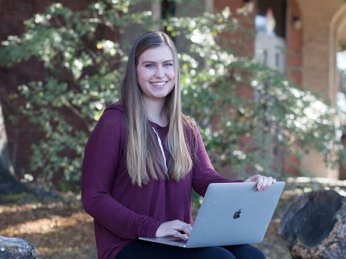 Smiling woman, seated with laptop, outdoors