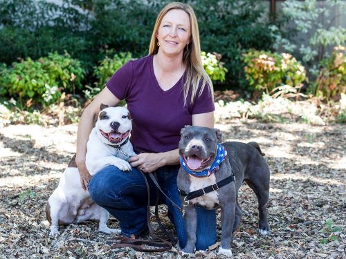 Woman kneeling, outdoors, flanked by two dogs